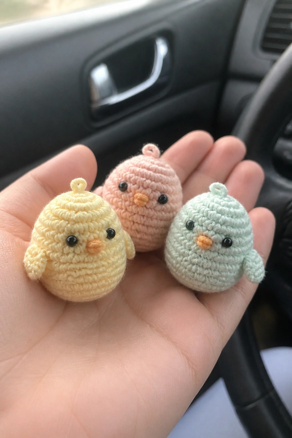 Three small crocheted birds in yellow, pink, and mint green held in a hand.