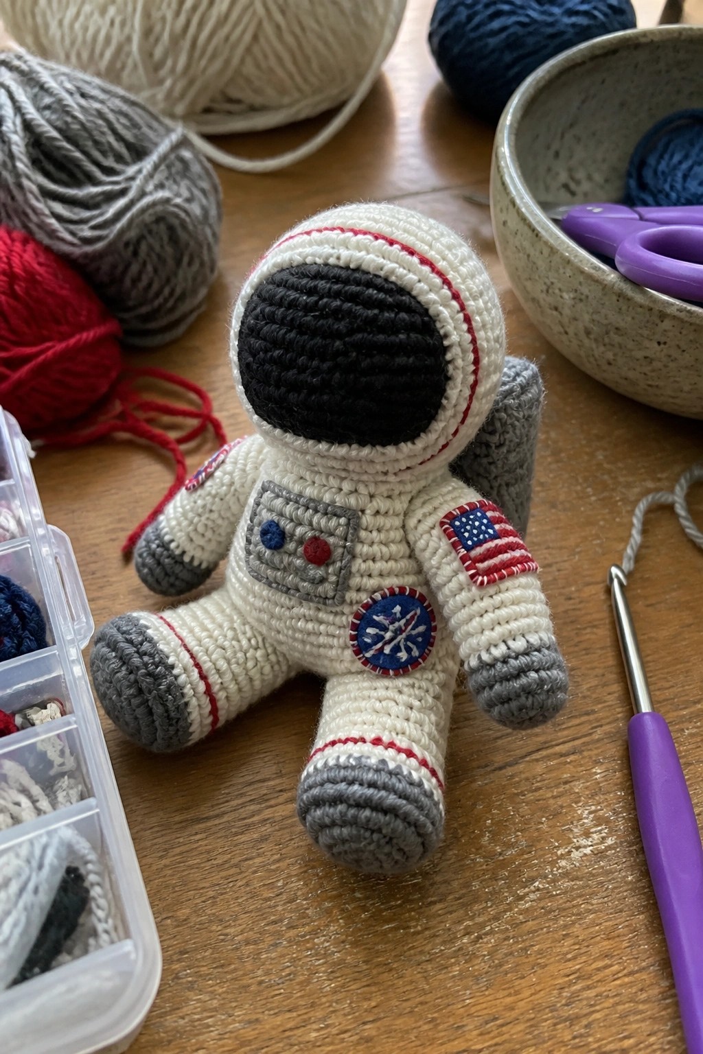 Crocheted white astronaut doll with flag patches amid yarn balls and tools