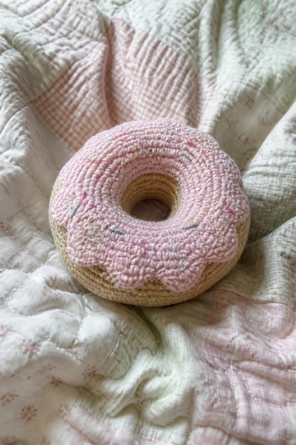Pink crocheted donut with sprinkles on a floral quilted blanket