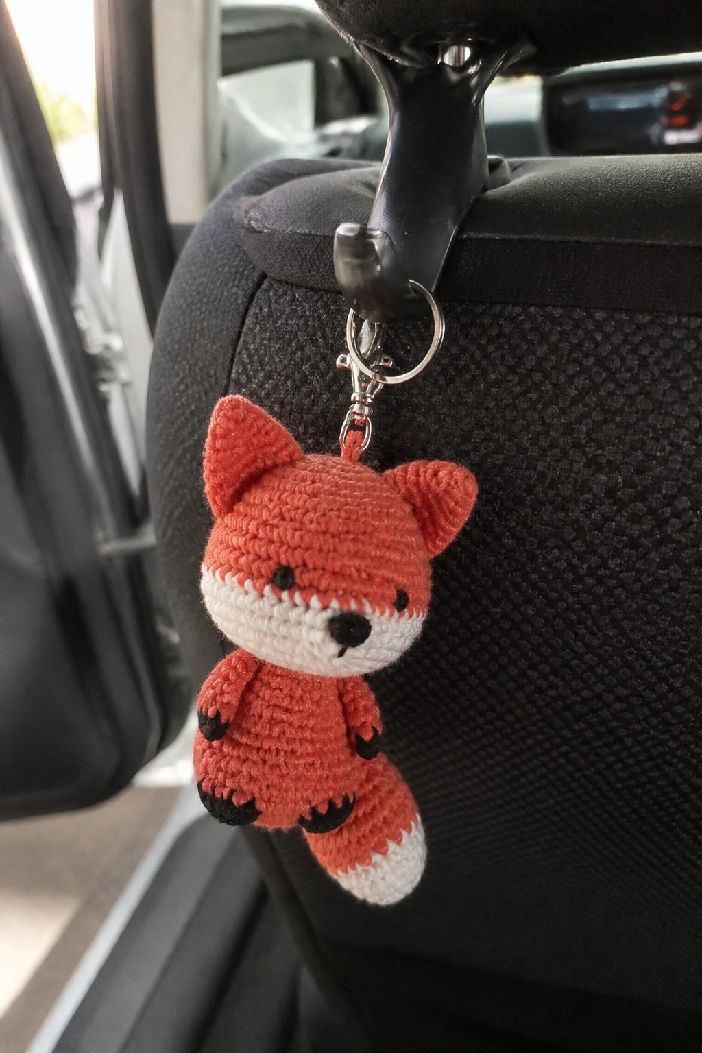 Crocheted orange fox keychain with white muzzle hanging from black car headrest