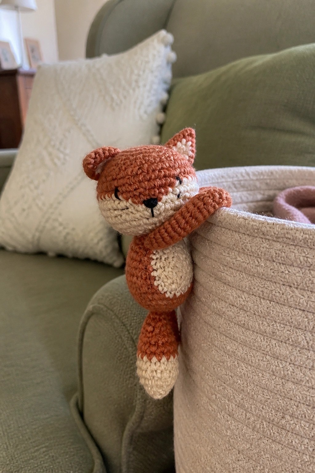 Crocheted orange fox toy peeking over the edge of a woven basket on a green couch.