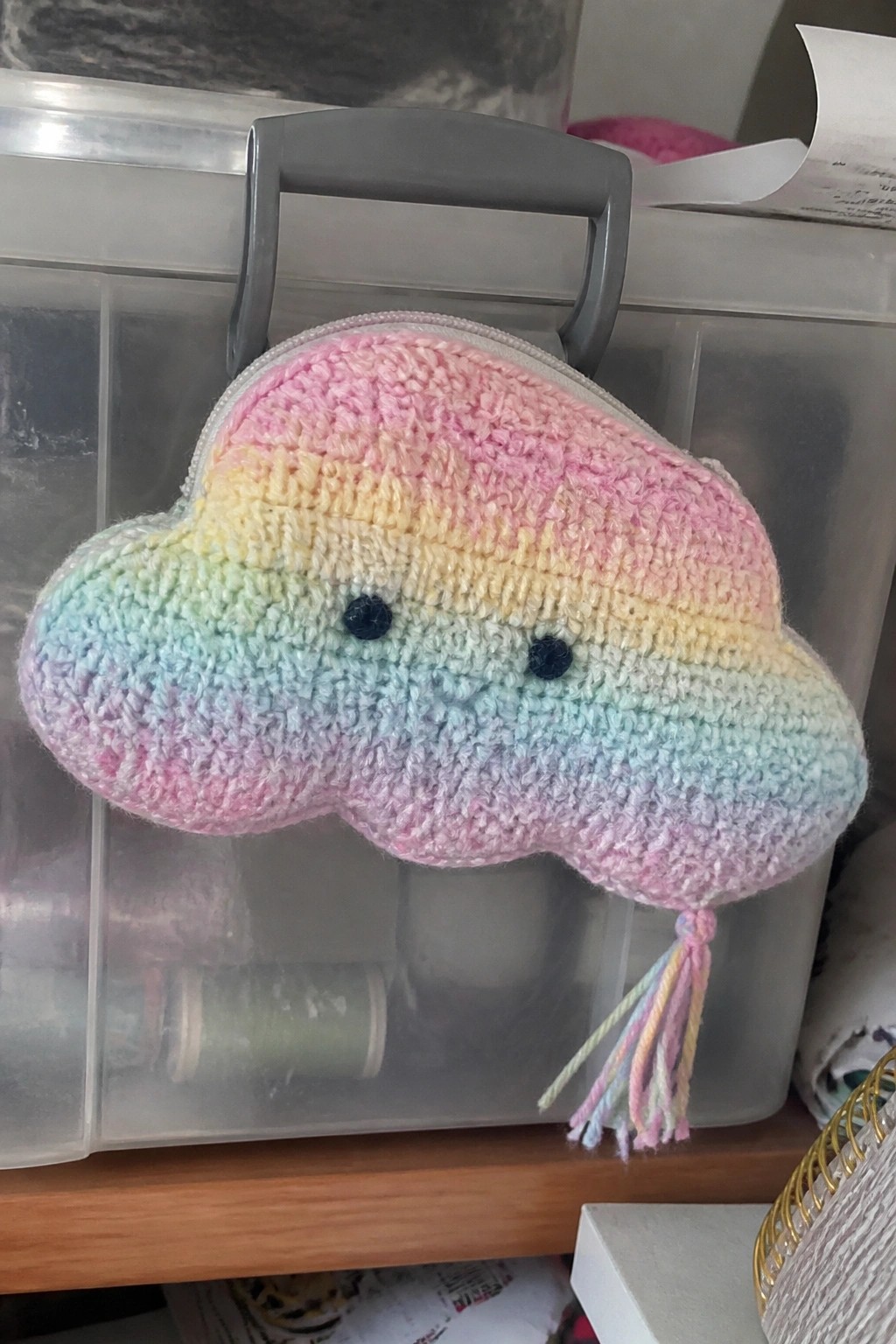 Rainbow crocheted cloud pouch with zipper, face, and tassel on bin handle