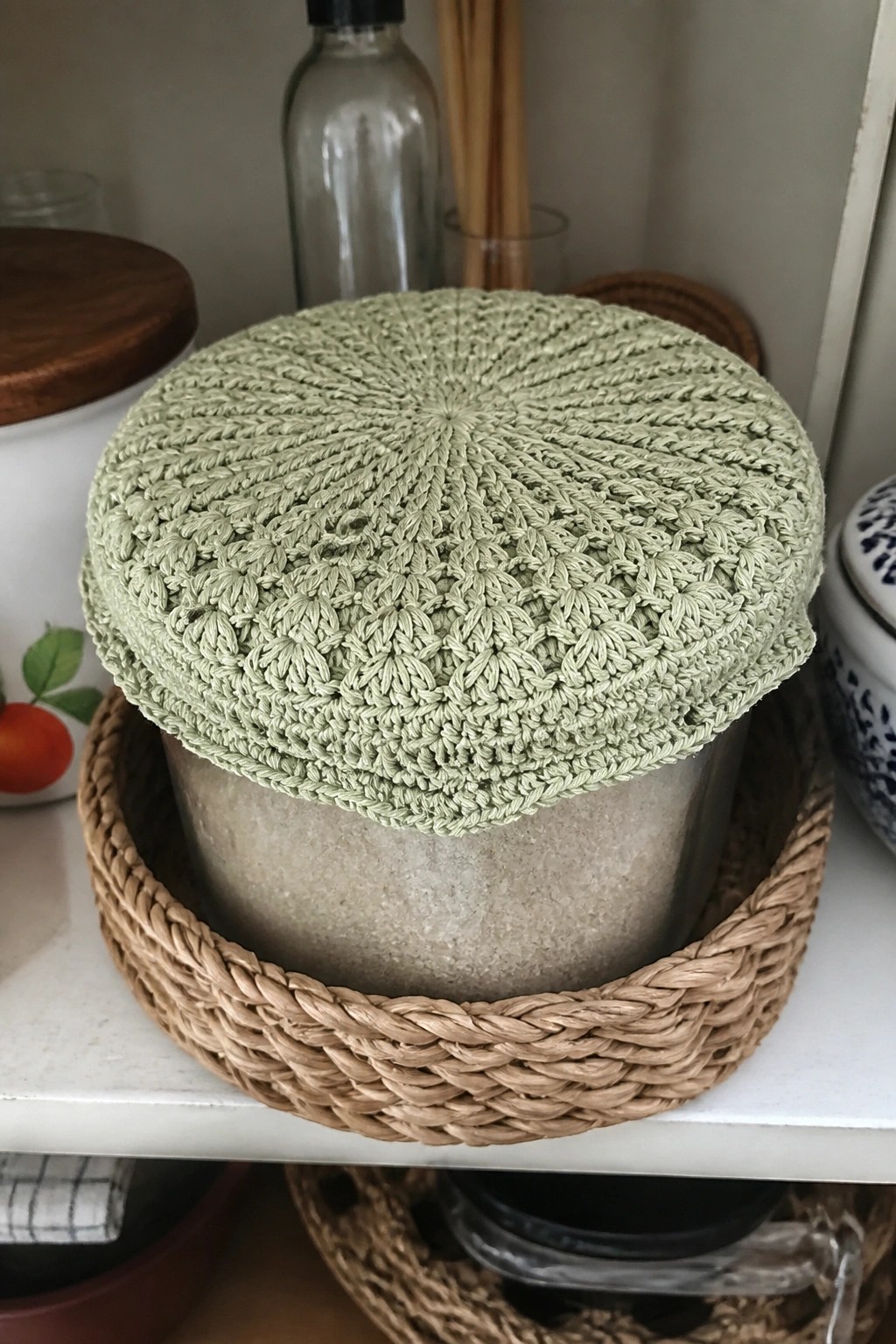 Light green crocheted cover on glass jar in woven basket on shelf.