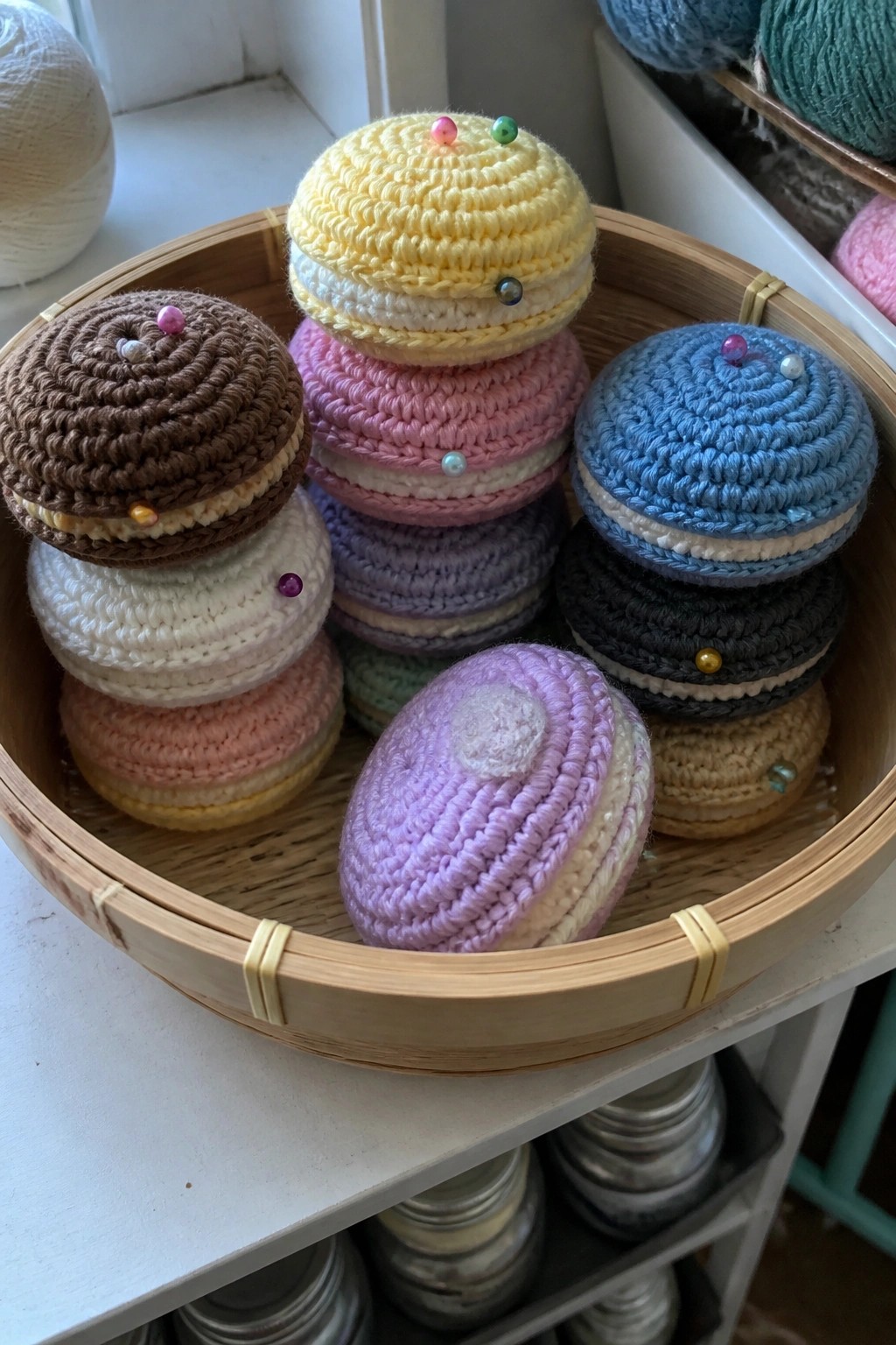 Colorful crocheted macaron pincushions stacked in a bamboo steamer basket with pins