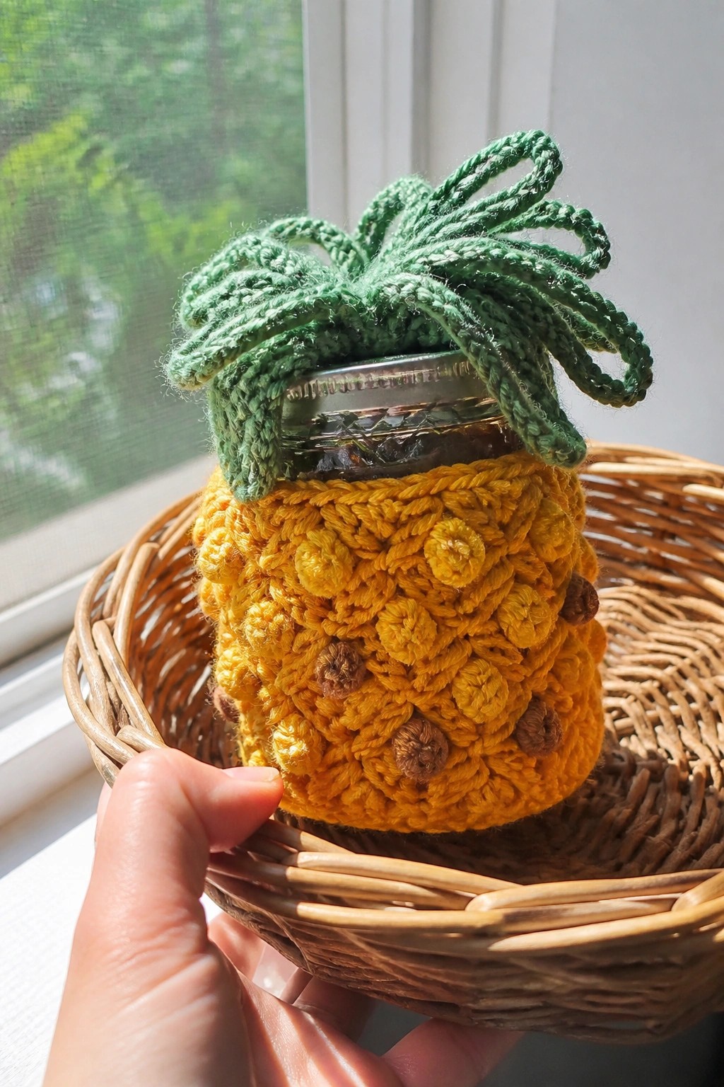 Hand holding wicker basket with yellow crocheted pineapple cozy on glass jar