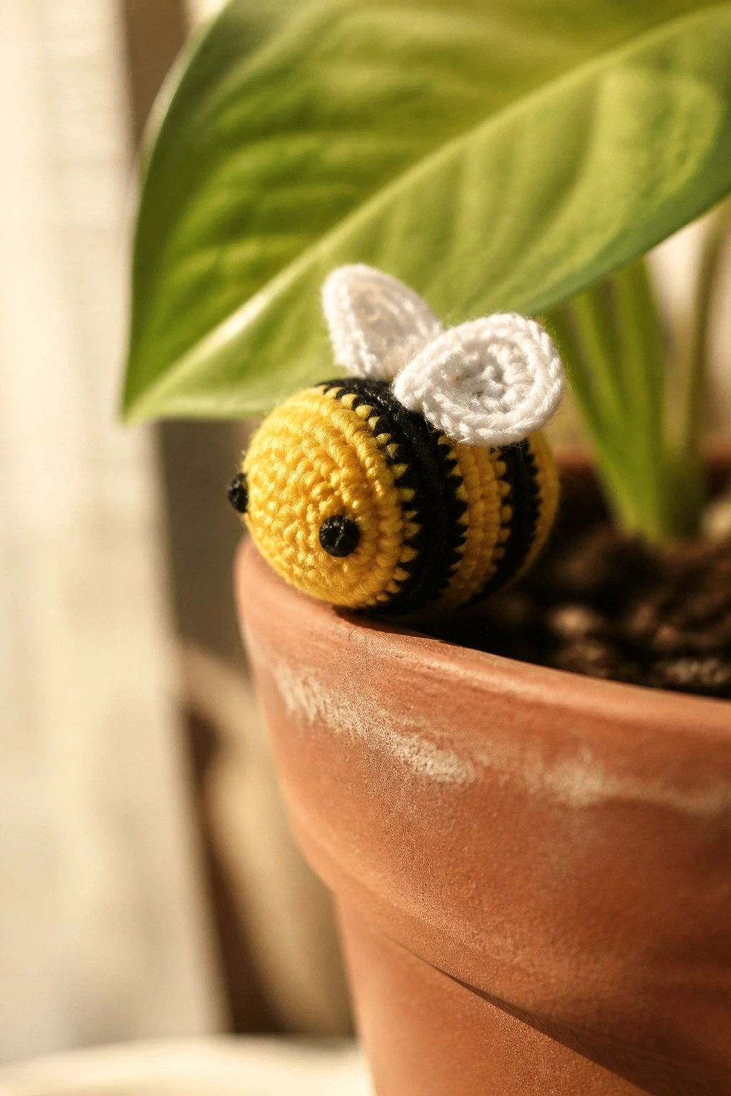 Crocheted yellow and black striped bee with white wings on terracotta pot