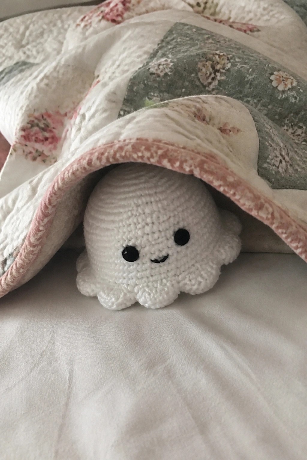 White crocheted octopus toy peeking from under a floral patchwork quilt