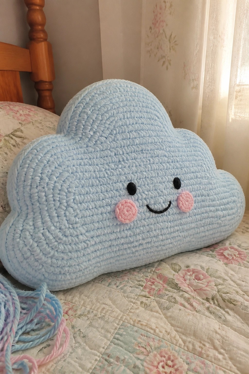 Light blue crocheted cloud pillow with smiling face on floral quilted bedspread