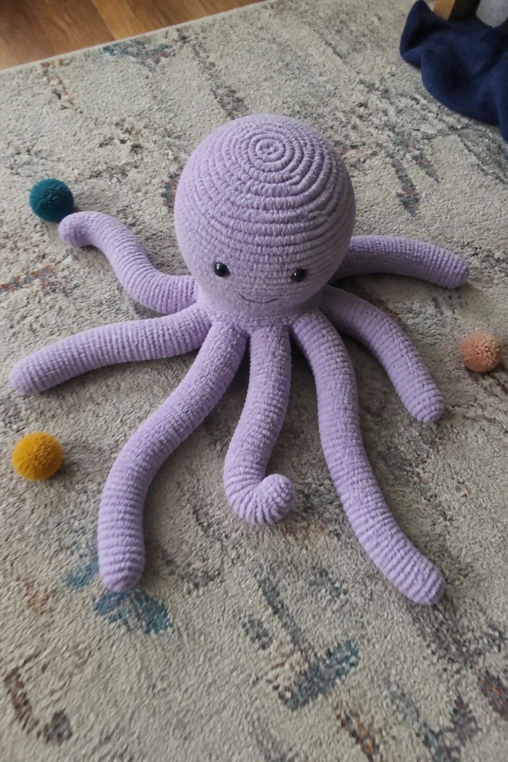 Purple crocheted octopus toy on patterned rug with colorful pom-poms