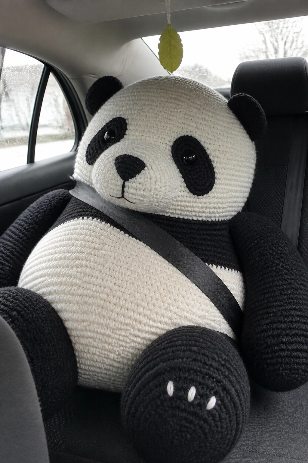 Large black-and-white crocheted panda secured by seatbelt in car seat