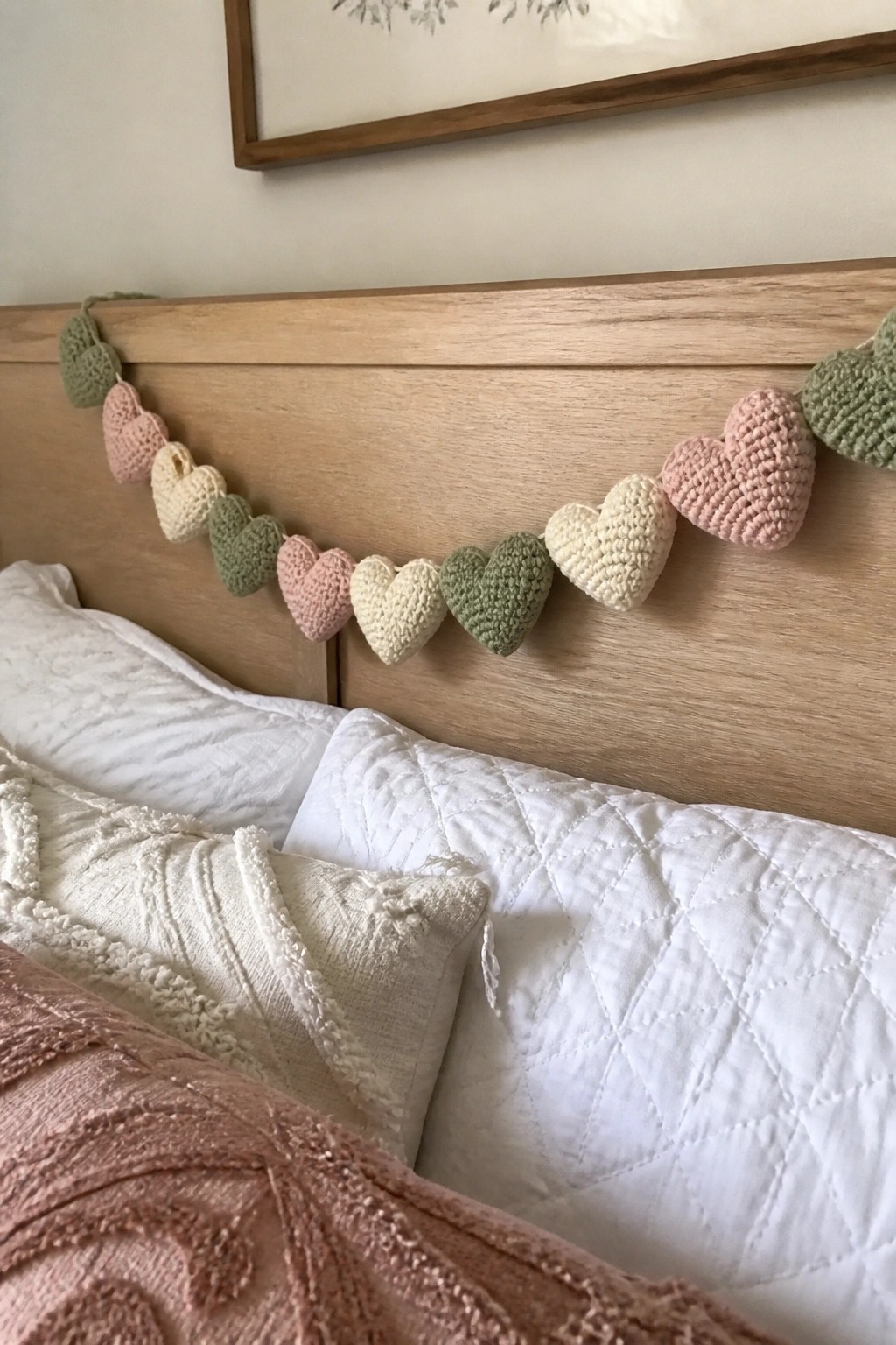 Pastel crocheted heart garland draped on wooden headboard above white pillows and bedding