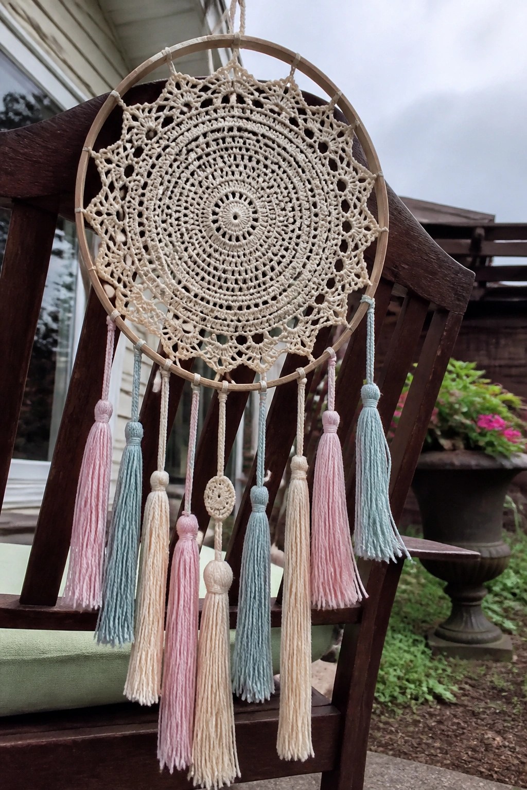 Crocheted beige dreamcatcher with pastel tassels on wooden chair outdoors