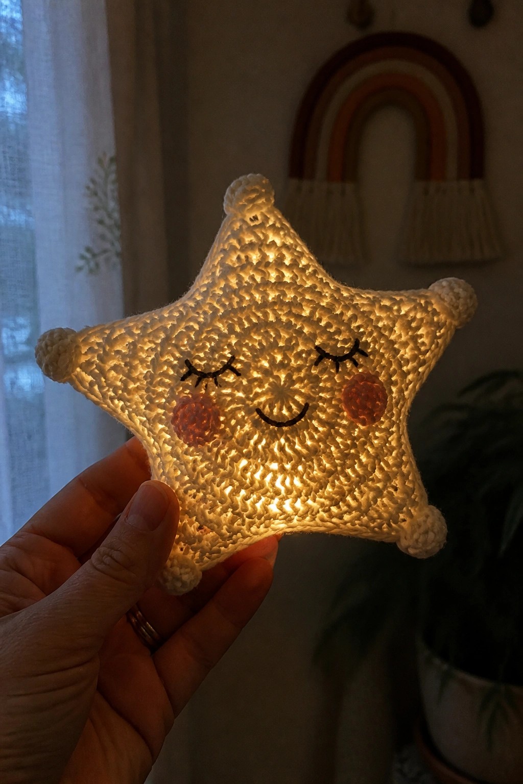 Hand holding glowing crocheted star with smiling face and rosy cheeks