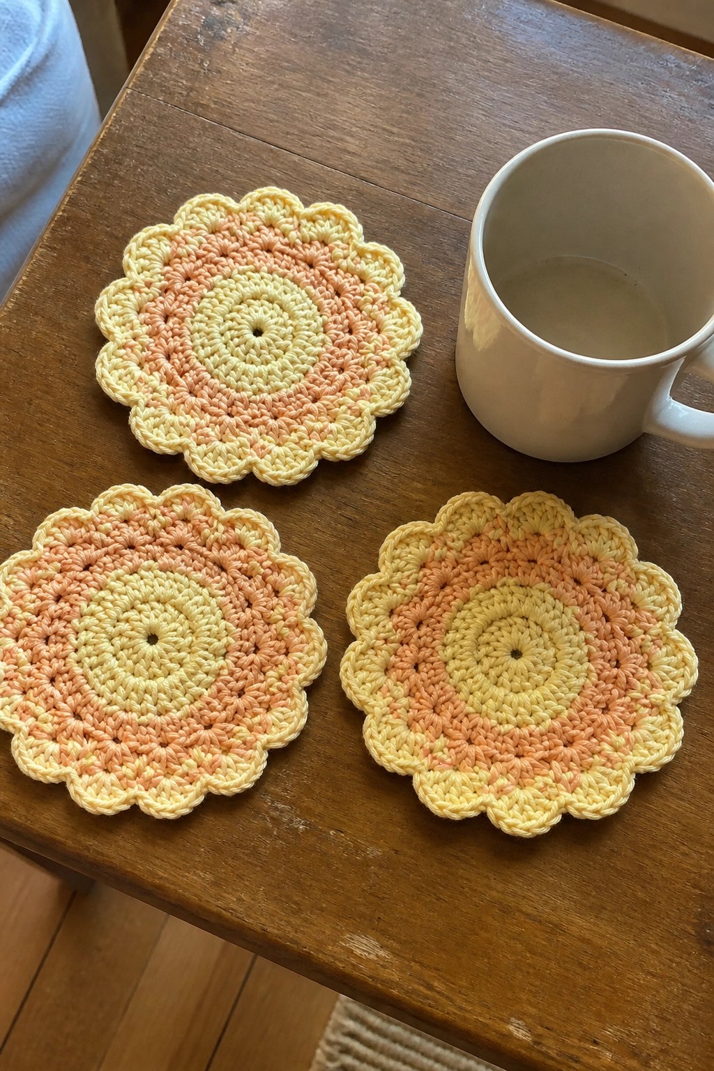 Three pastel crocheted coasters beside a white mug on a wooden table