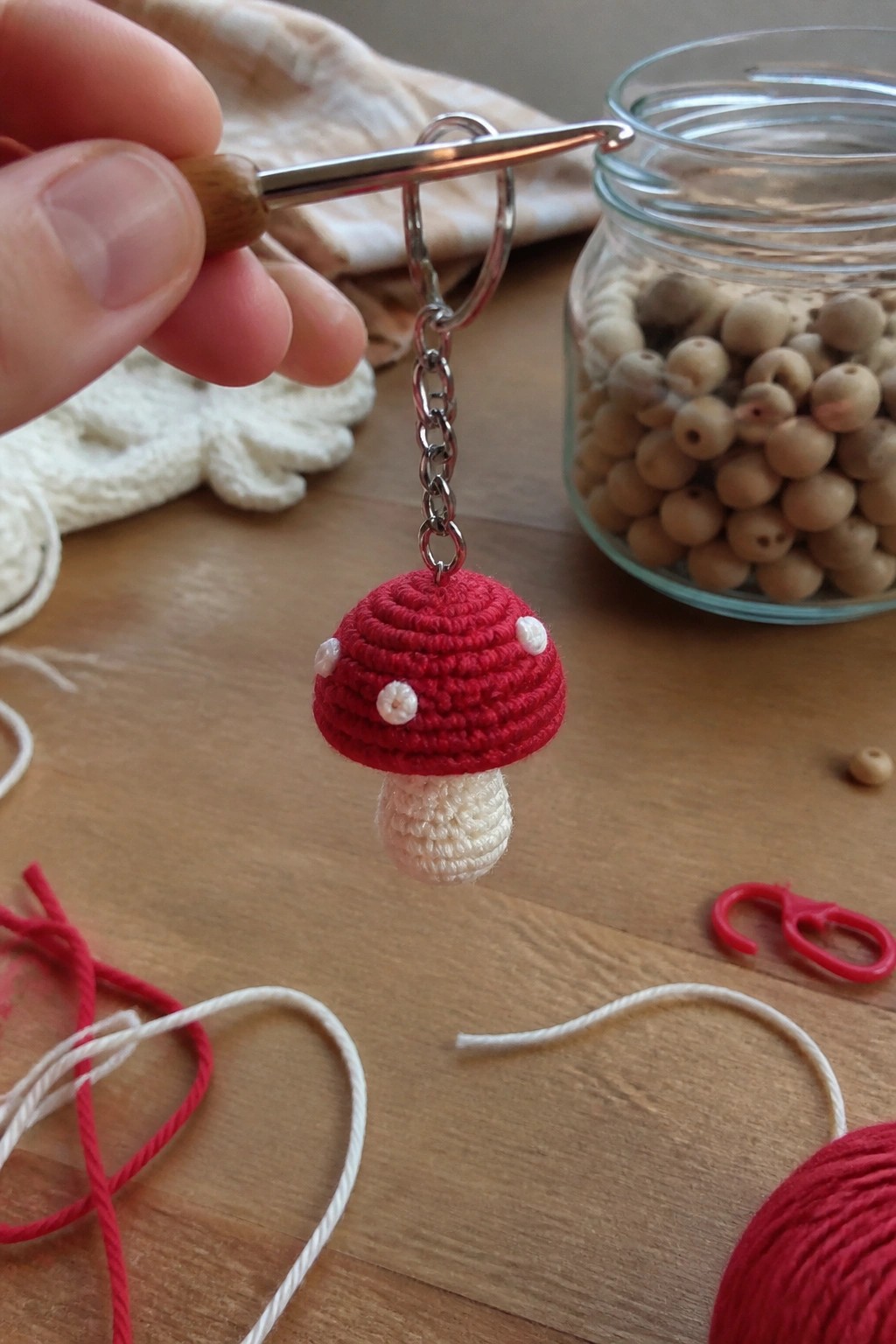 Hand holding crochet hook with red mushroom keychain dangling from chain