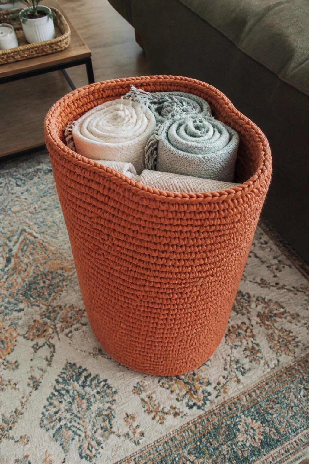 Orange woven basket holding rolled white, beige, and blue blankets on rug