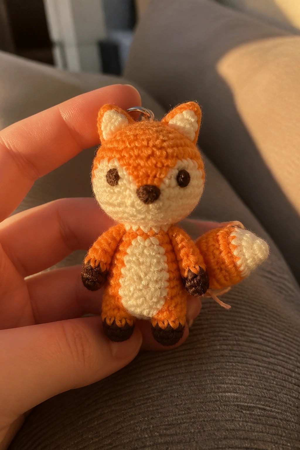 Hand holding small orange crocheted fox keychain with white belly and fluffy tail.