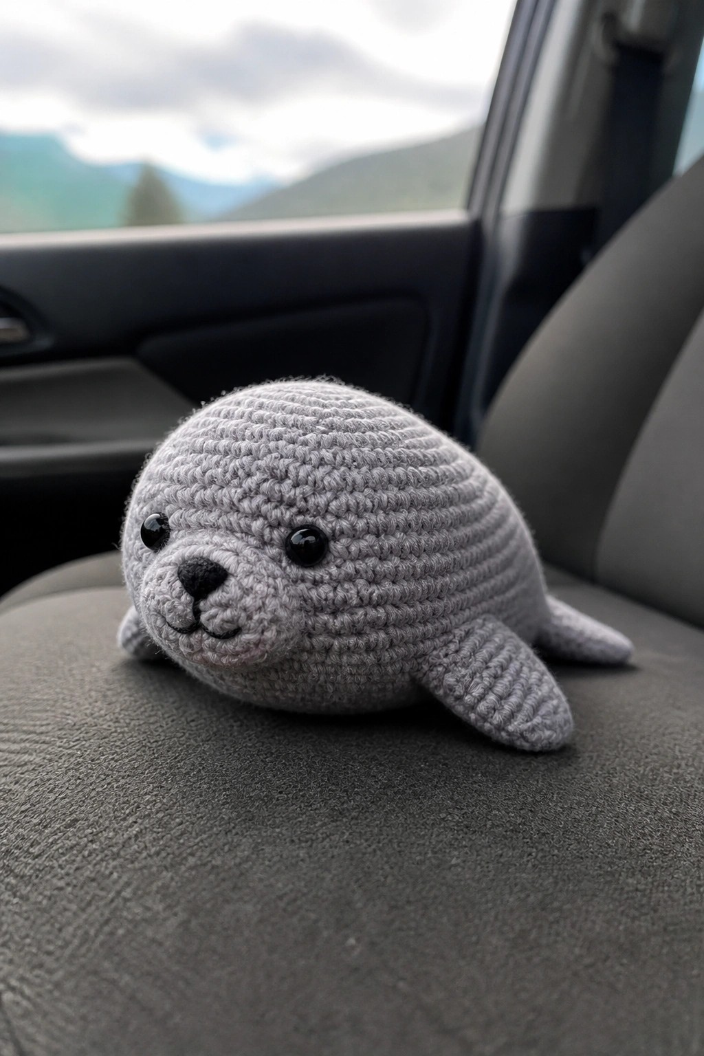 Gray crocheted seal plush on car seat with mountains visible through window