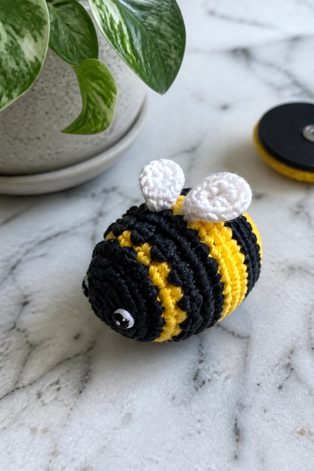 Crocheted yellow and black striped bee with white wings on marble surface