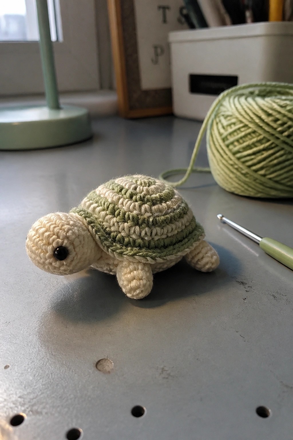 Crocheted beige and green turtle beside yarn ball and hook on gray table.