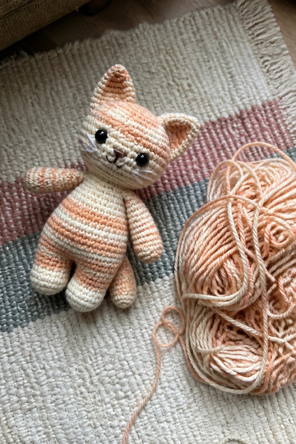 Crocheted peach striped cat toy beside matching yarn ball on woven rug