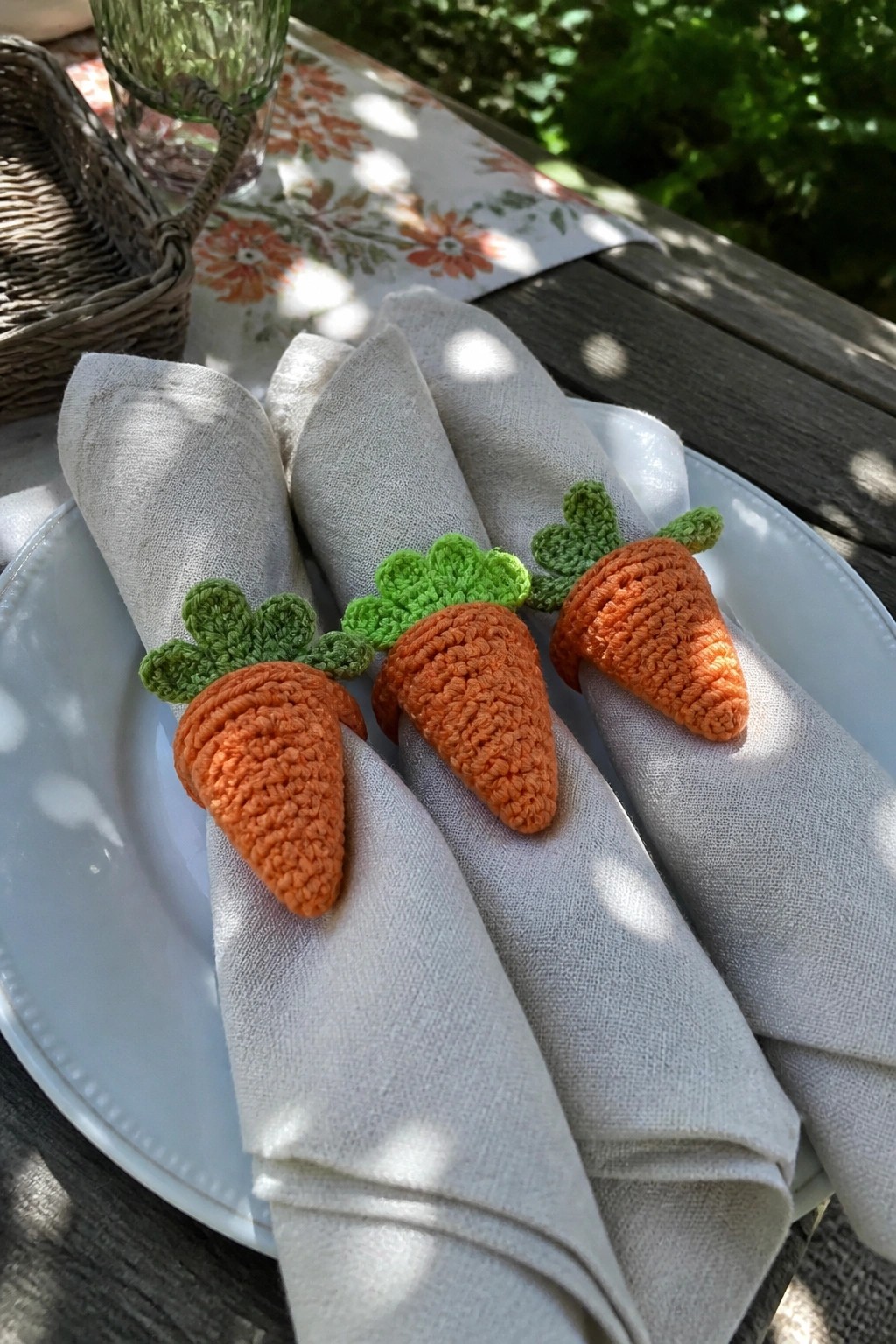 Three gray napkins with crocheted orange carrot rings on white plates outdoors