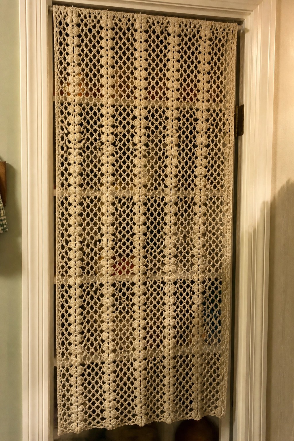 Beige crocheted lace curtain with circular patterns hanging in white doorway