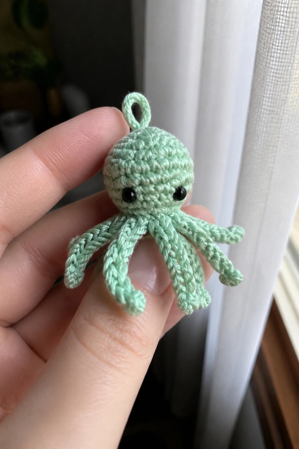 Fingers holding a small mint green crocheted octopus with black eyes and tentacles.