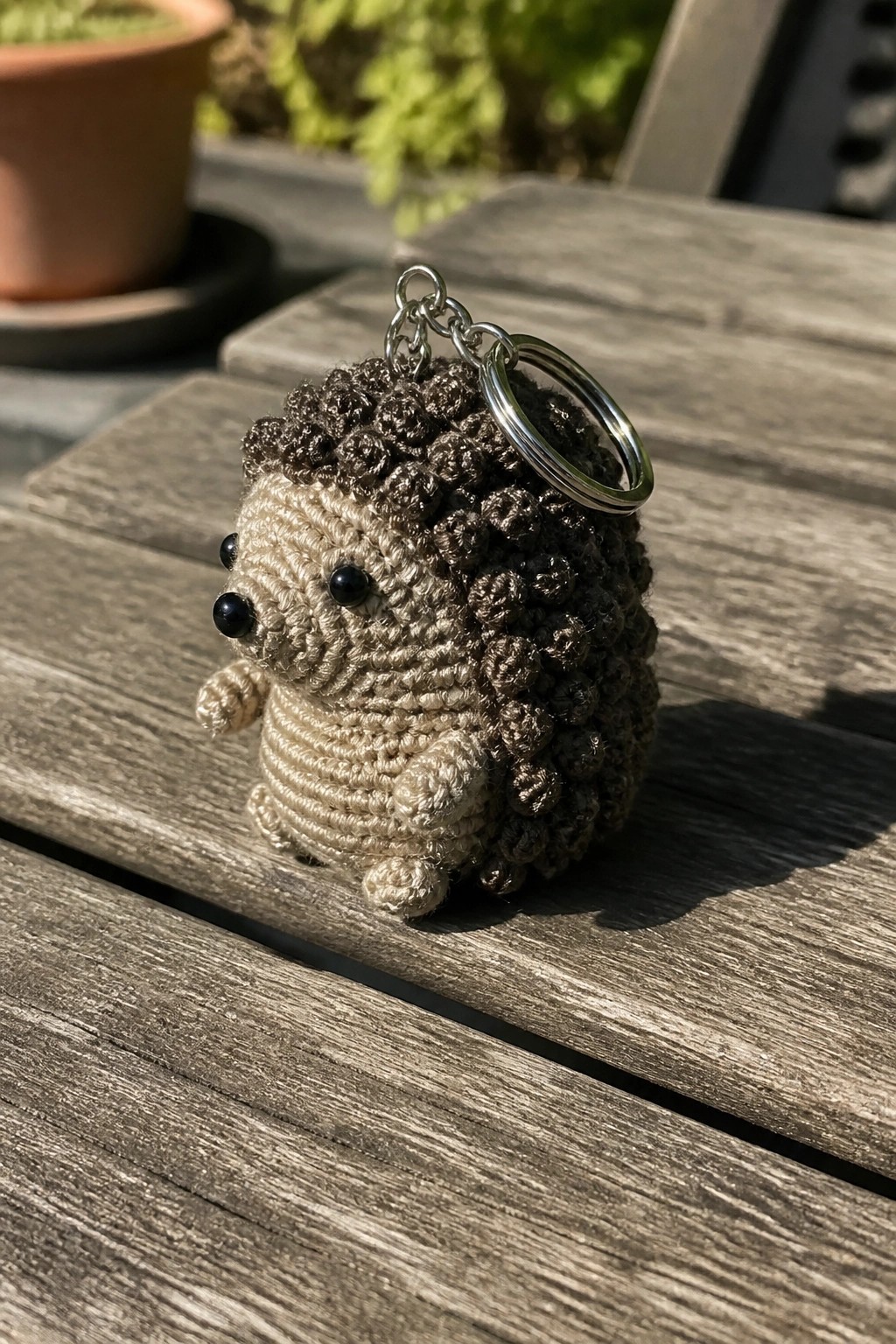 Crocheted hedgehog keychain with beige body, brown spikes, and metal ring on wood.