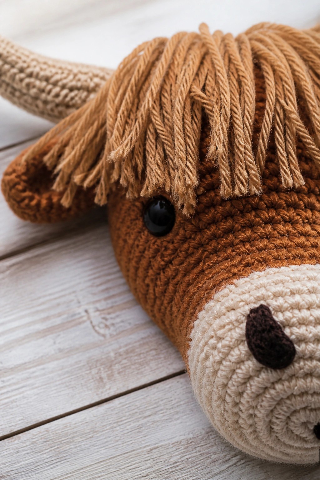 Close-up of crocheted brown Highland cow toy with shaggy mane, horn, and black eye.