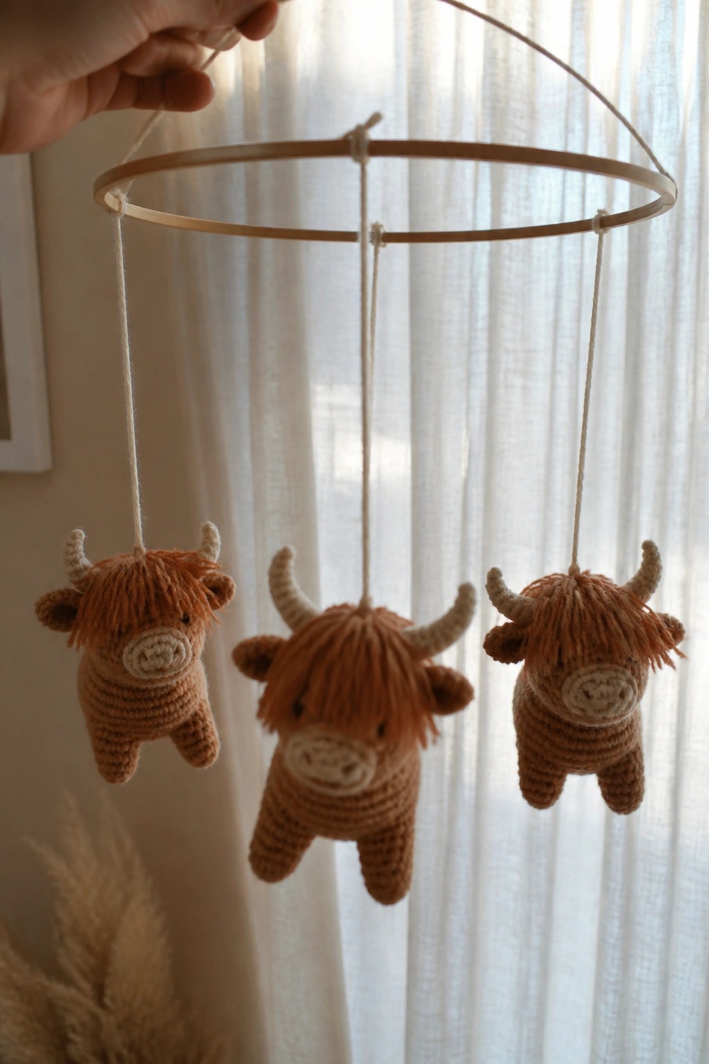 Hand holding wooden hoop mobile with three brown crocheted Highland cows hanging