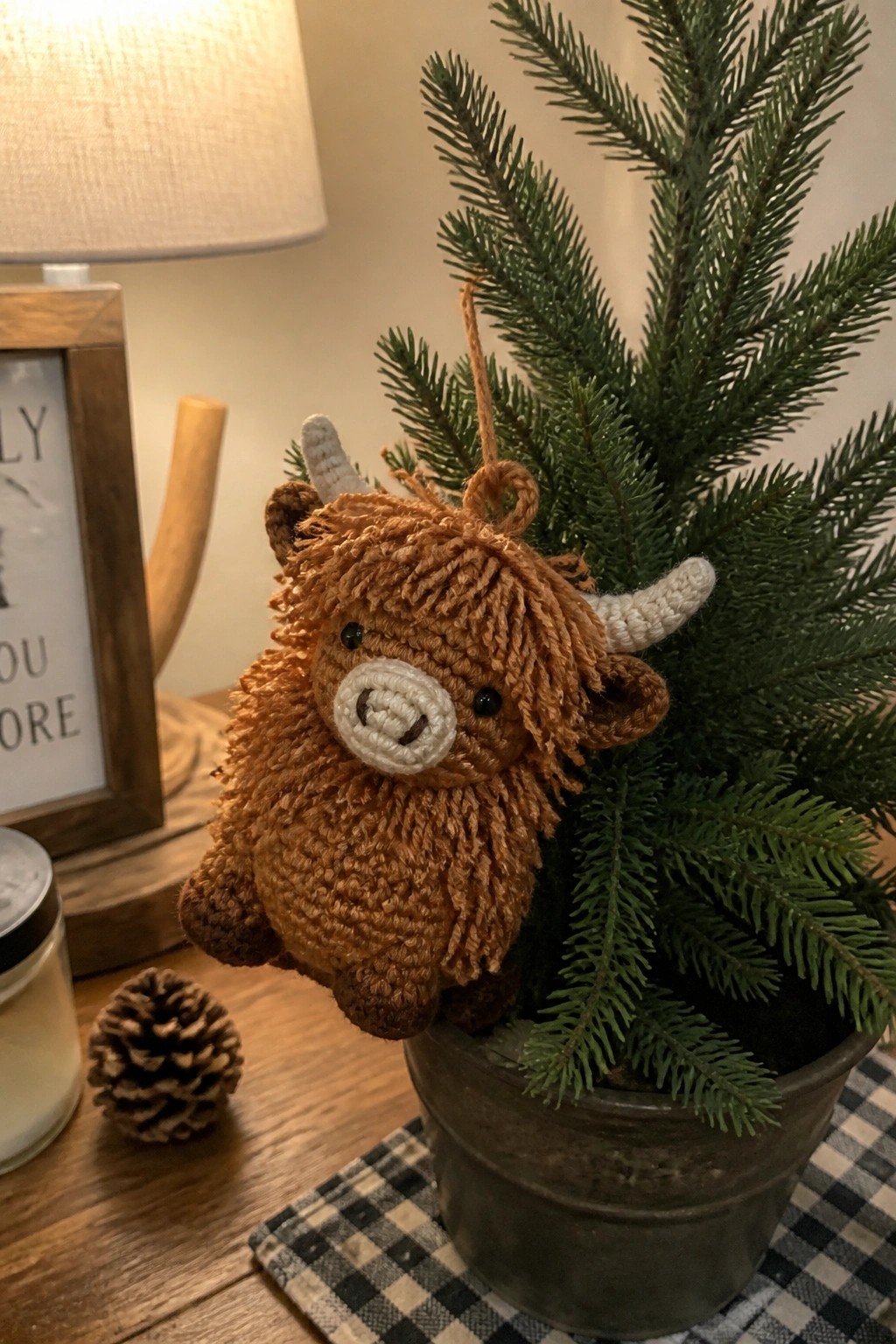 Brown crocheted Highland cow ornament hanging on small potted Christmas tree.