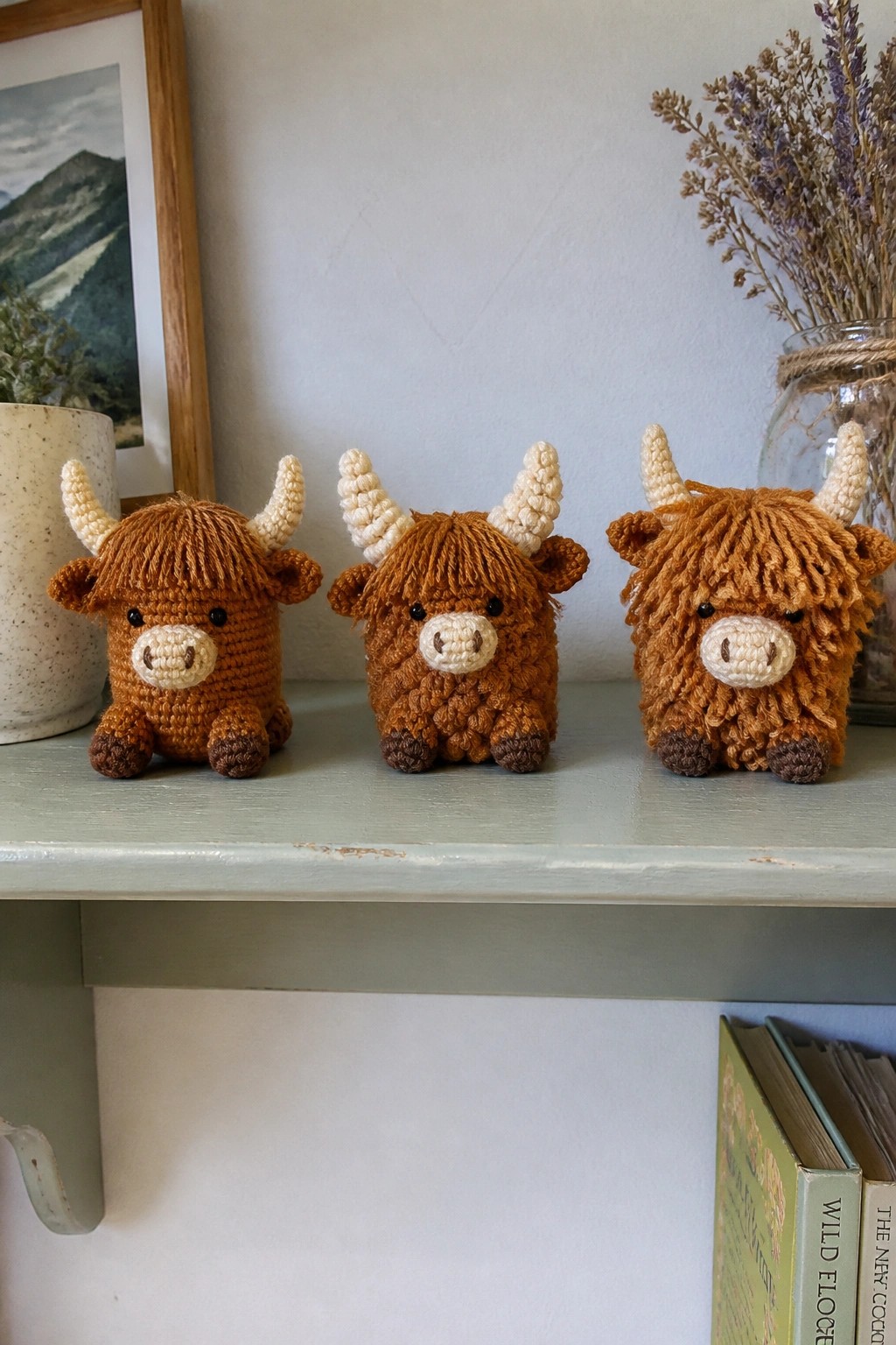 Three crocheted Highland cows with horns on a light green shelf