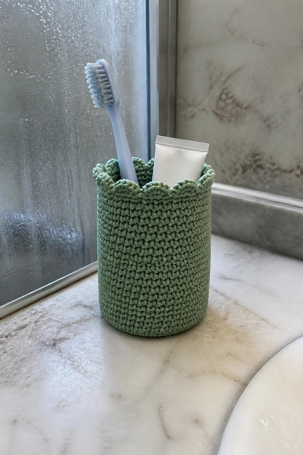 Green crocheted holder with blue toothbrush and white tube on marble counter