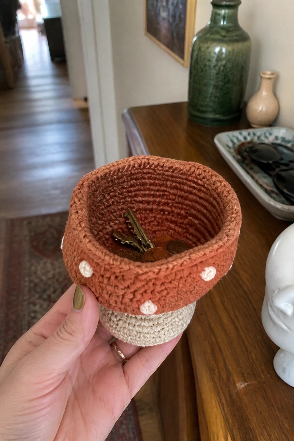 Hand holding orange crocheted basket with white dots, keys, and coins.