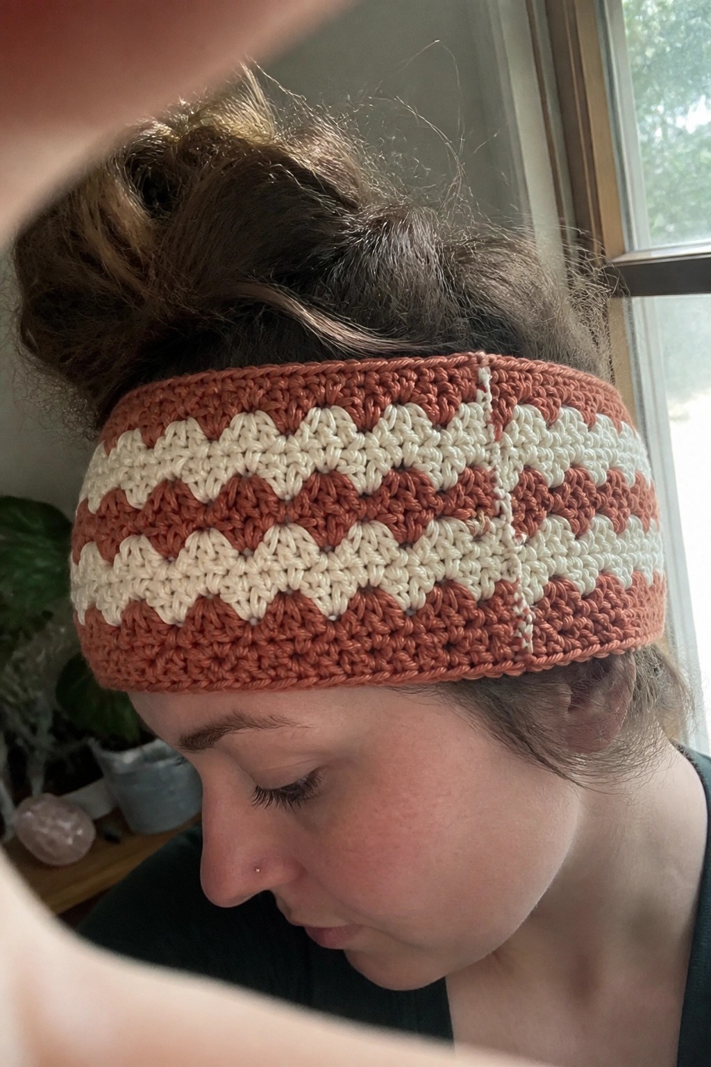 Woman with bun wearing crocheted rust-orange and cream zigzag headband in profile.