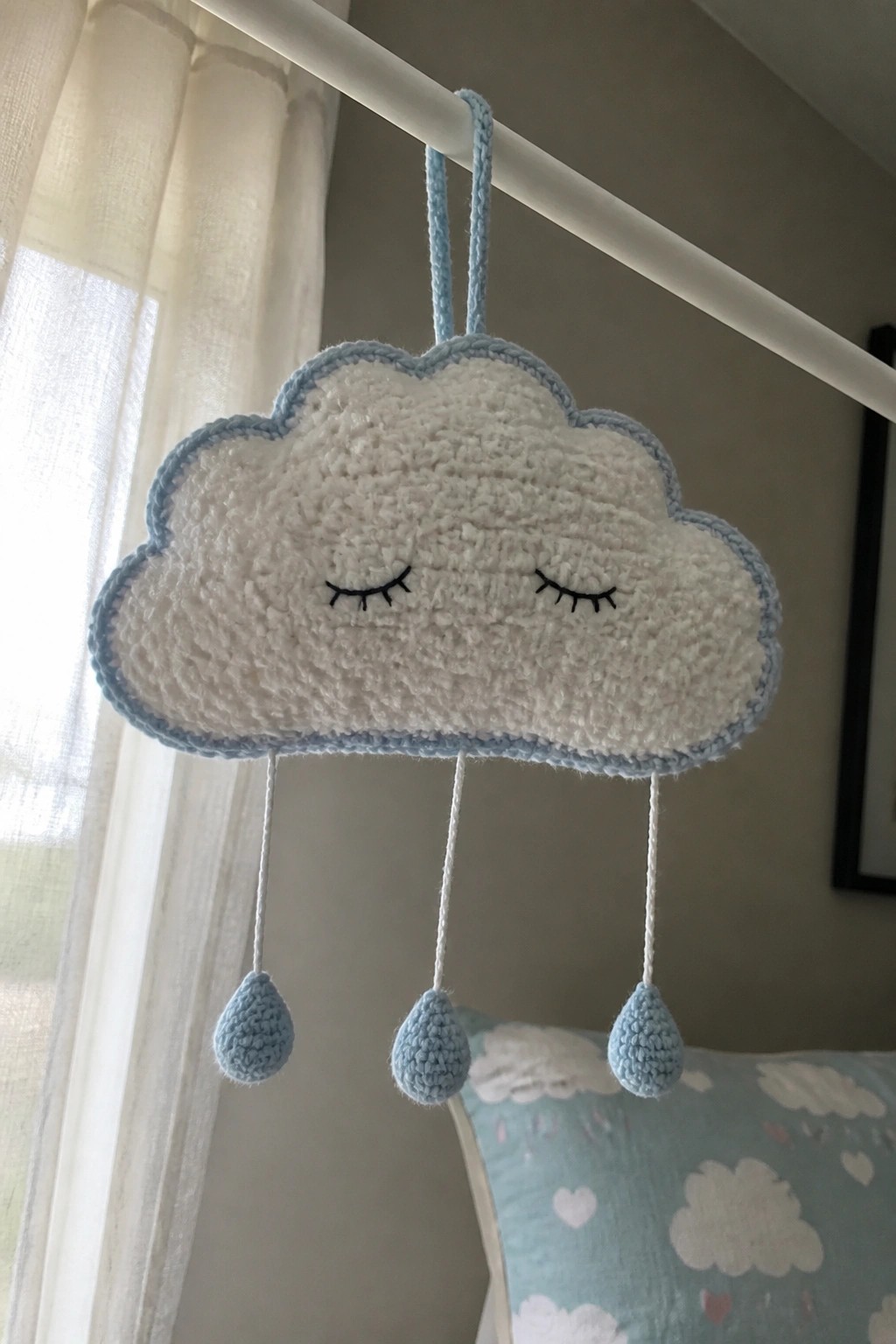 Crocheted white cloud with blue trim, sleepy eyes, and three hanging blue raindrops.