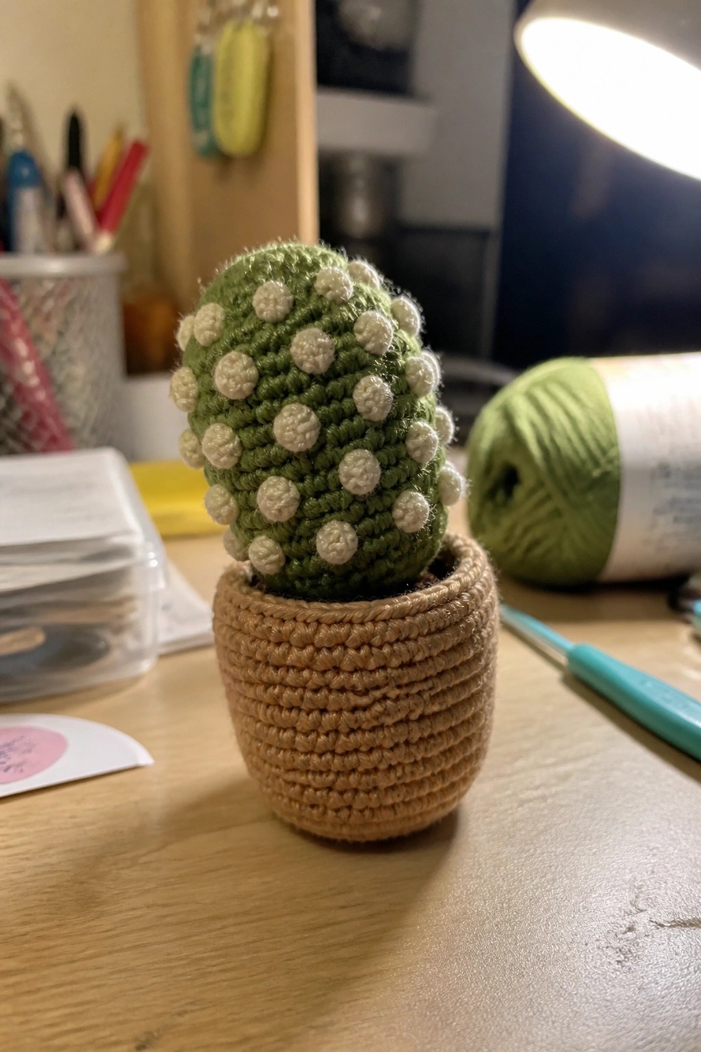 Crocheted green cactus with white dots in tan yarn pot on wooden desk