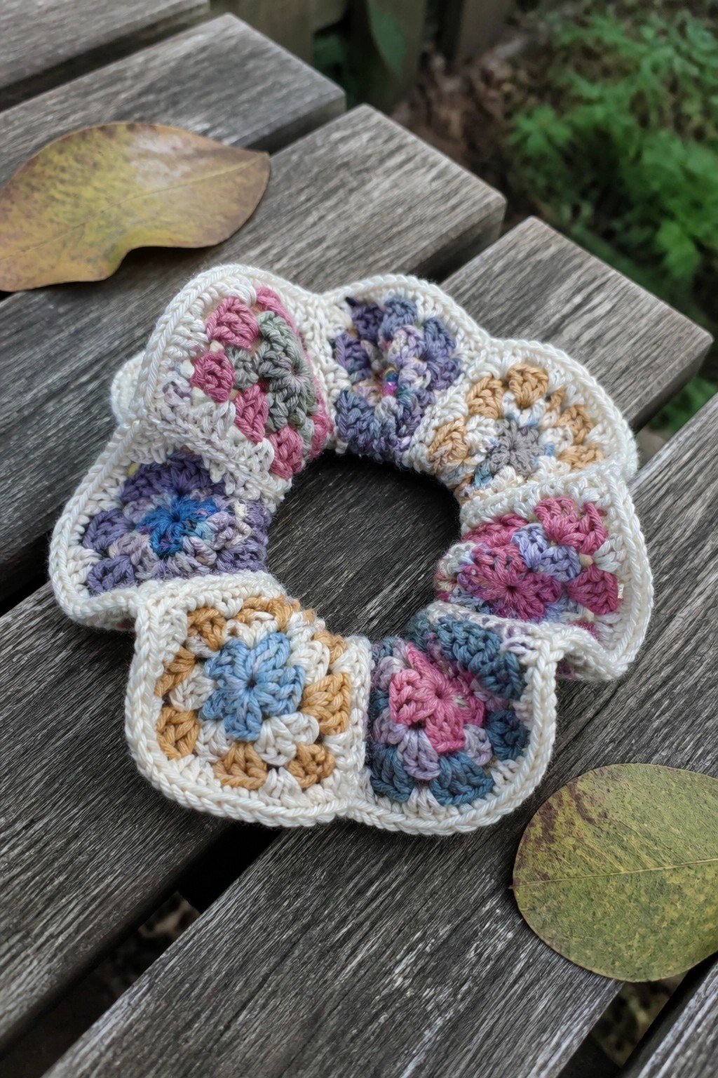 Multicolored granny square crochet scrunchie on weathered wooden table with leaves