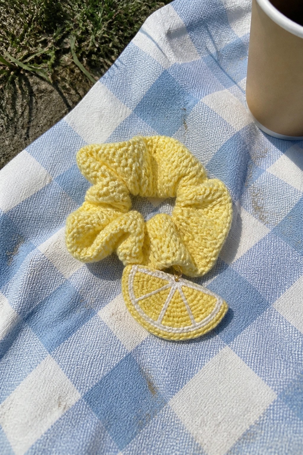 Yellow knitted scrunchie with lemon slice charm on blue checkered blanket