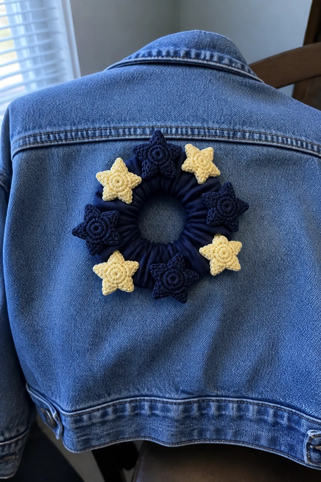 Blue denim jacket back with navy scrunchie and yellow-blue crocheted stars.