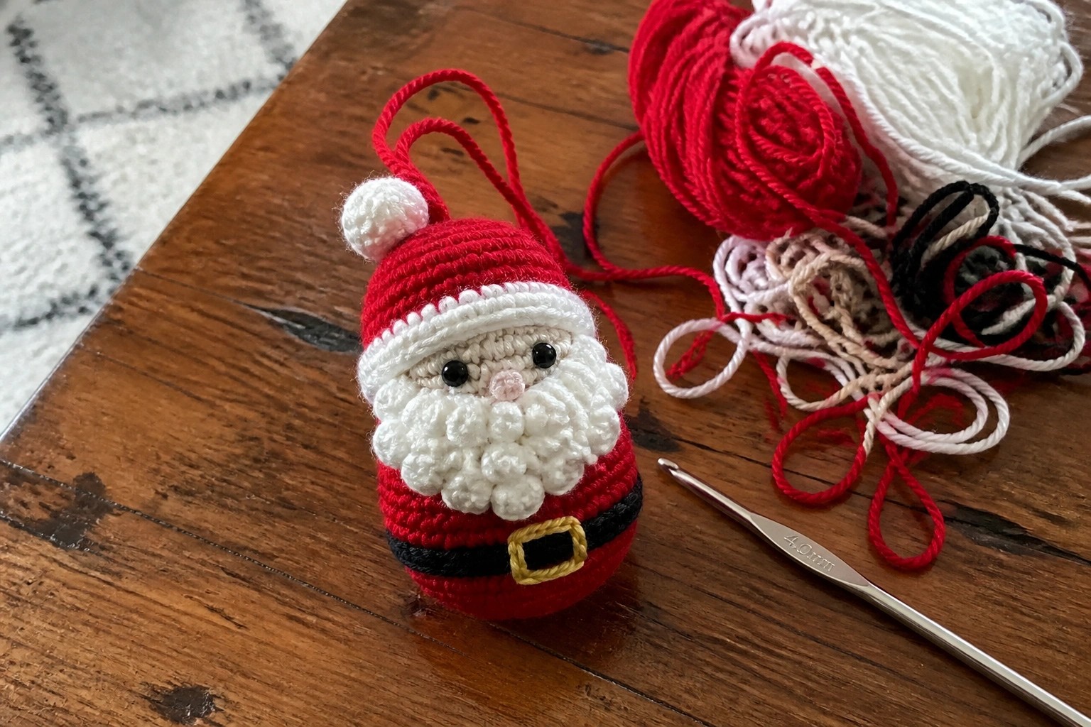 Crocheted Santa Claus ornament with beard beside red yarn and crochet hook on table