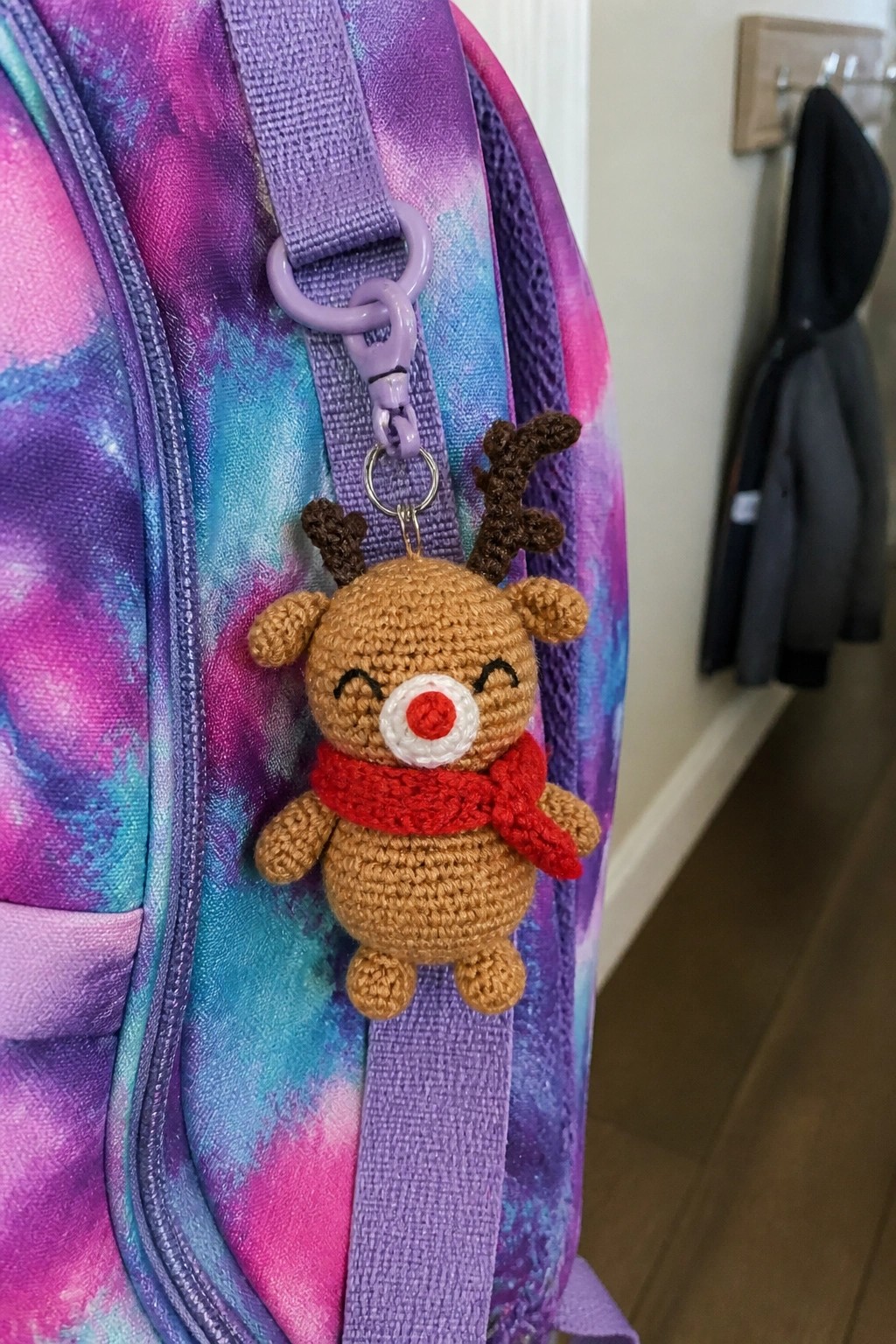 Crocheted reindeer keychain with red scarf on purple tie-dye backpack strap.