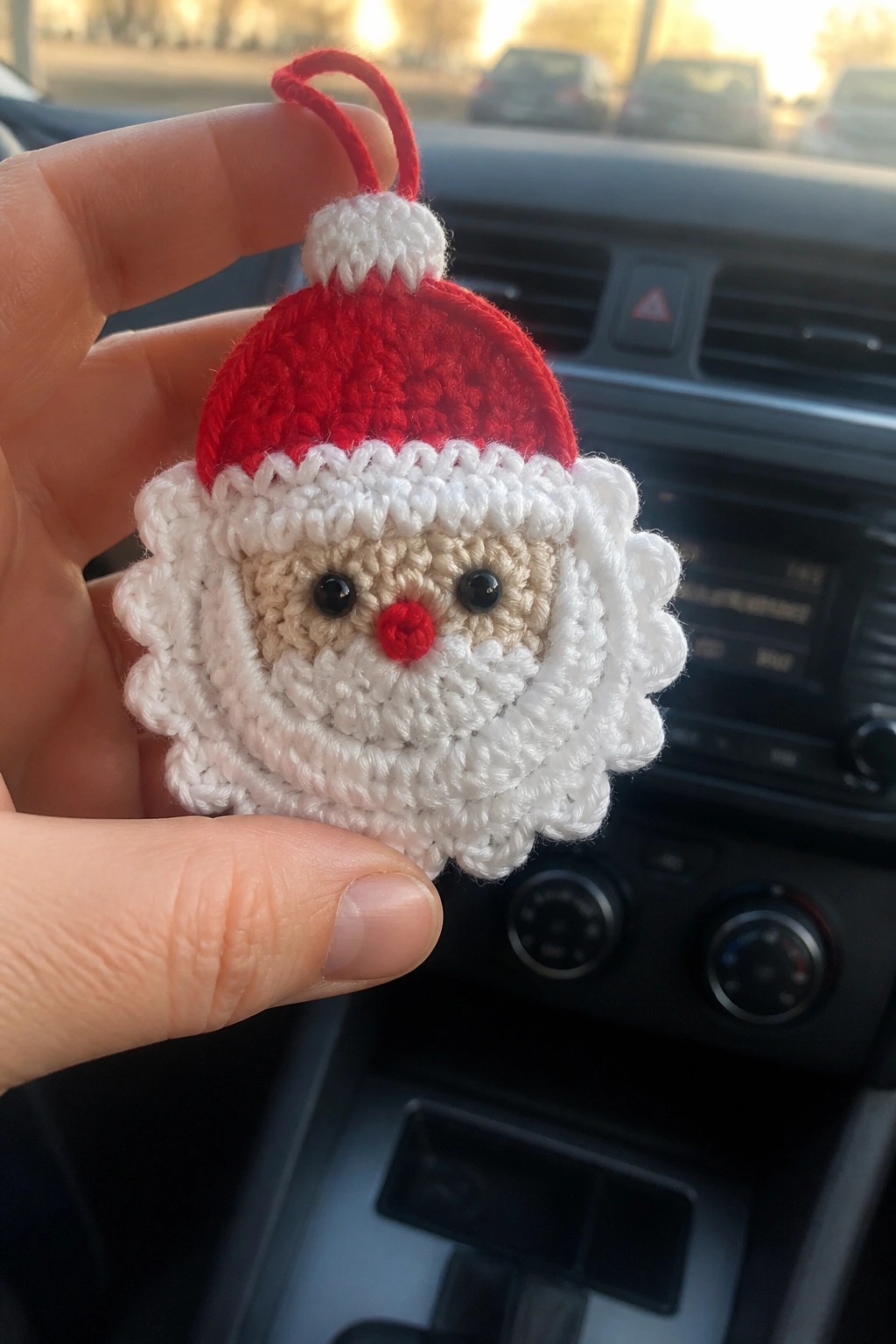 Hand holding crocheted Santa ornament with red hat, white beard in car.