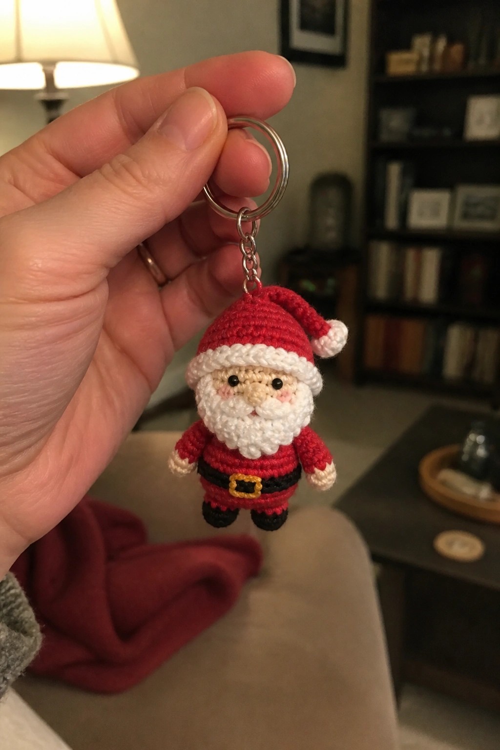 Hand holding crocheted Santa keychain in red suit, white beard, and black boots.