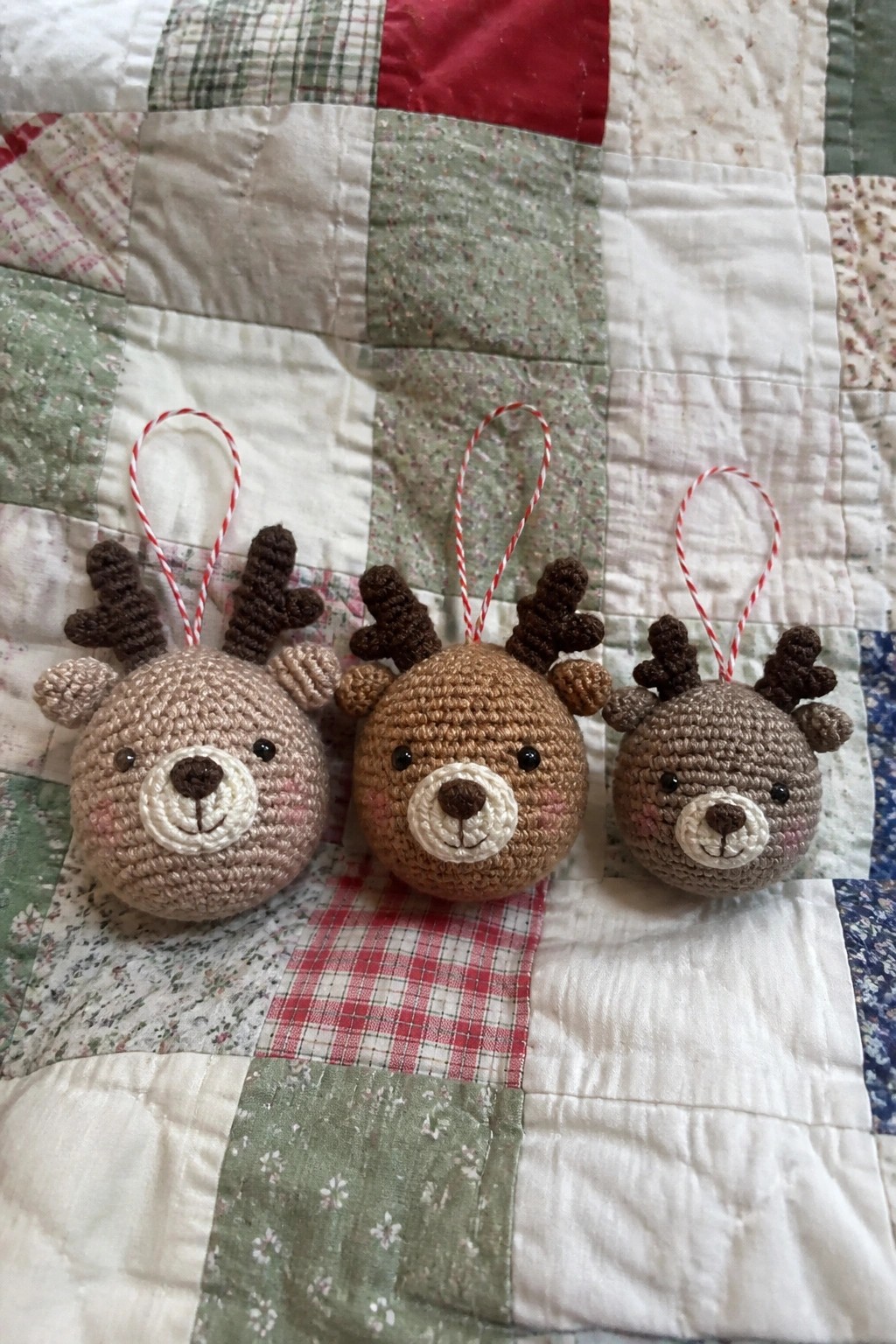Three crocheted reindeer ornaments in varying shades on a patchwork quilt.