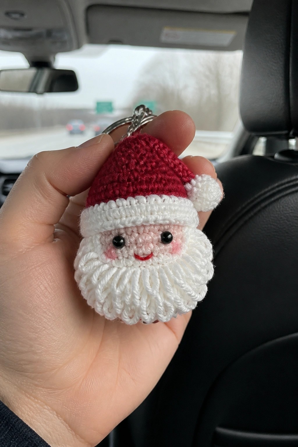 Hand holding crocheted Santa keychain with red hat and white beard in car