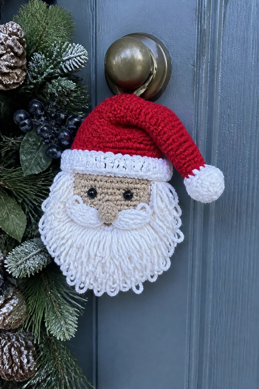 Crocheted Santa Claus ornament with red hat and white beard on blue door beside wreath