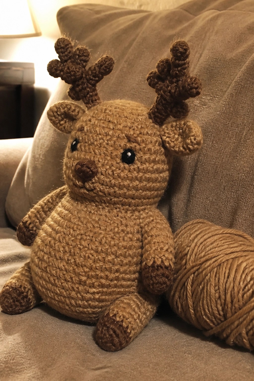 Crocheted brown reindeer plush toy with antlers beside a ball of yarn on a couch