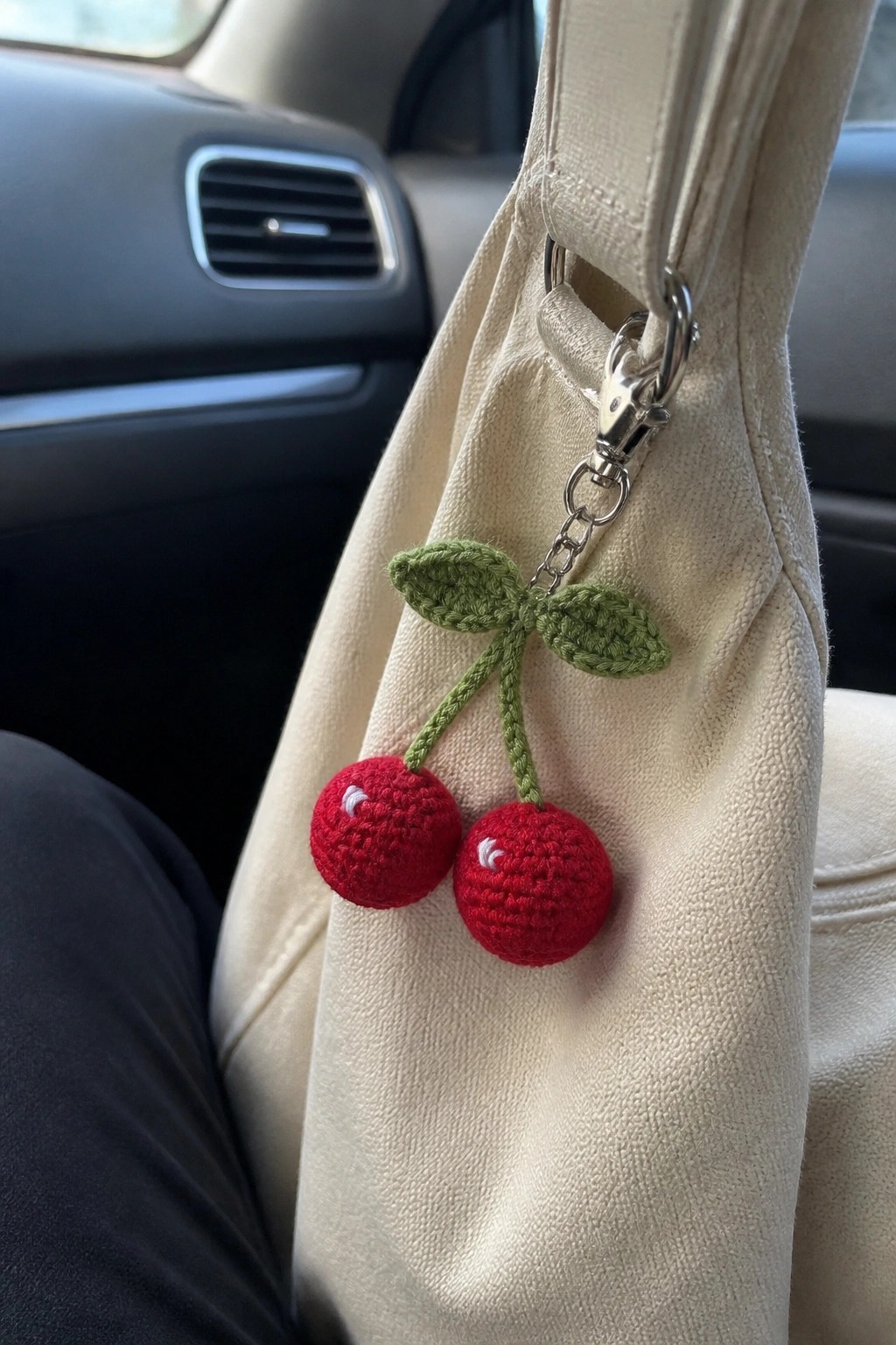 Crocheted red cherry keychain with green leaves on beige bag in car